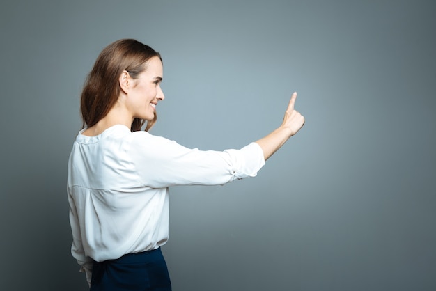 Activité intéressante. Ravie de belle femme positive tenant son bras et souriant tout en regardant son index