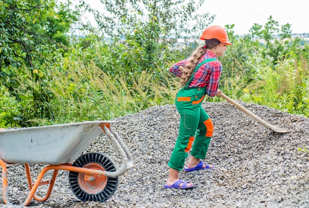 Activité de plein air. fille qui transporte des décombres dans une brouette. les travaux de construction. fille constructeur prend une pelle de gravats. jeunesse travailleuse. jeu de constructeur et de construction.