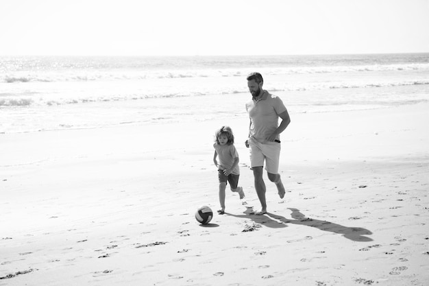 Activité sportive père et fils jouent au football ou au football sur la plage papa avec enfant garçon le jour d'été