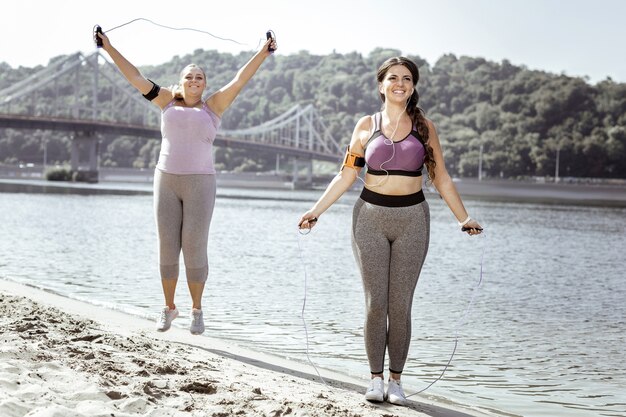 Activité utile. Des femmes positives ravies utilisant des cordes à sauter en sautant sur la plage