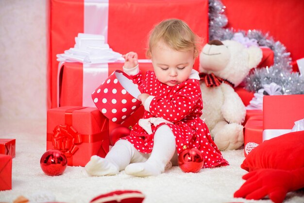 Activités à faire avec les tout-petits à Noël. Cadeaux pour enfant premier noël. Une petite fille joue près d'une pile de coffrets cadeaux. Vacances en famille. Activités de Noël pour les tout-petits. Cadeaux de Noël pour tout-petit.