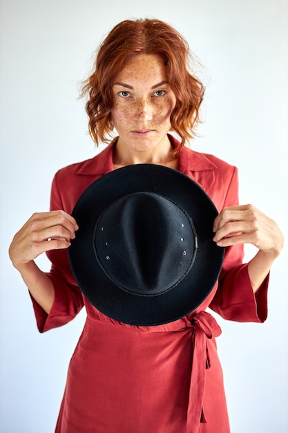 L'actrice élégante tient un chapeau noir dans les mains posant, ayant un regard confiant mystérieux