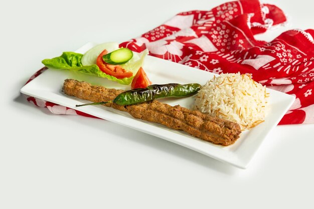 Adana kebab de style turc avec du riz et de la salade dans un plat isolé sur une nappe colorée vue latérale sur fond gris