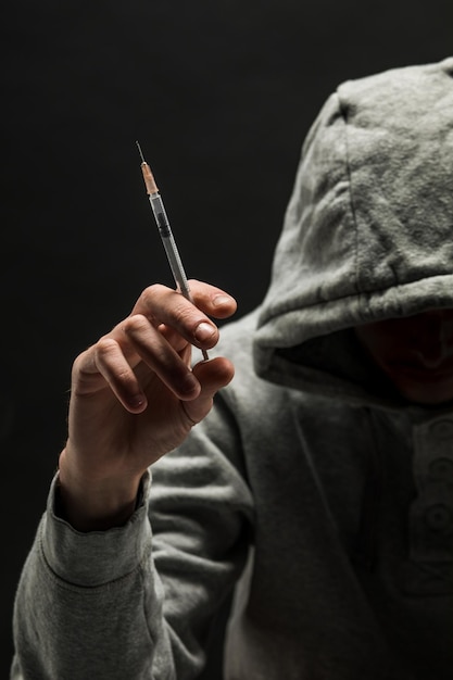 Addict en sweat à capuche gris sur la tête souffre de dépendance sur un fond noir foncé