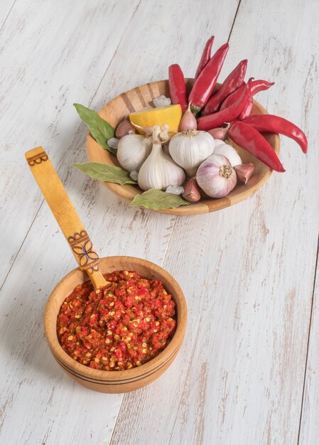 Adjika chaud fait maison à partir de piments avec des épices sur une table en bois blanc.