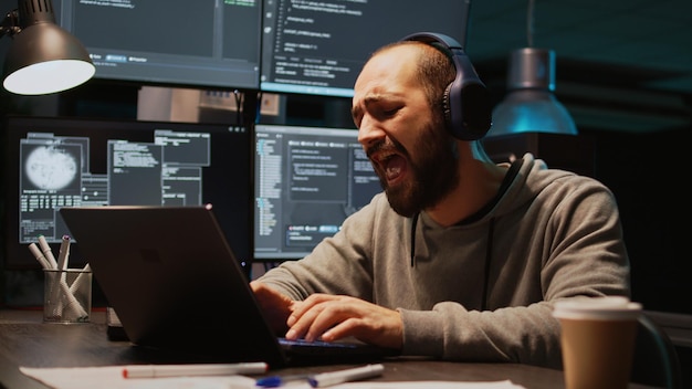 L'administrateur de la base de données s'amuse à écouter de la musique sur un casque, à chanter et à jouer de la batterie à air la nuit. Taper du code de programmation sur un ordinateur portable et s'amuser, se sentir joyeux. Prise de vue à main levée.