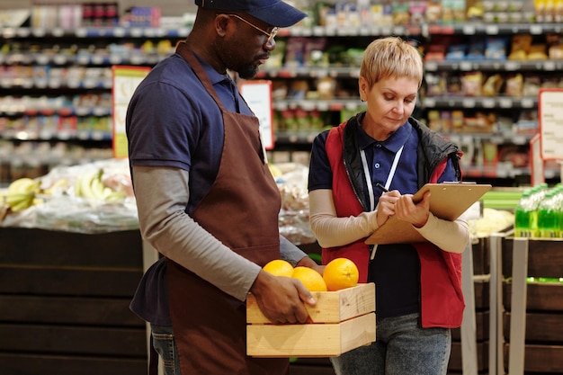 Administrateur d'un supermarché prenant des notes tout en se tenant à côté d'un assistant commercial