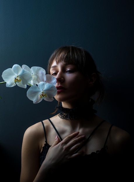 Ado romantique avec orchidée sur fond noir. Portrait de jeune femme charmante en fleurs. Jolie fille.