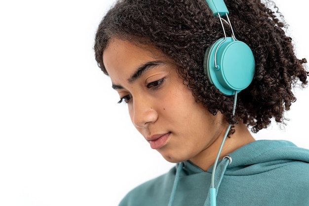 Adolescent afro-américain aux cheveux bouclés regardant vers le bas et écouter de la musique dans un casque turquoise moderne
