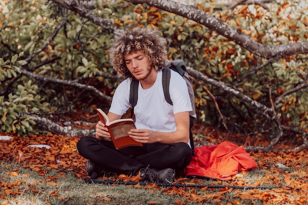 Un adolescent afro se détend en lisant un livre assis dans les bois par beau temps d'automne. Photo de haute qualité