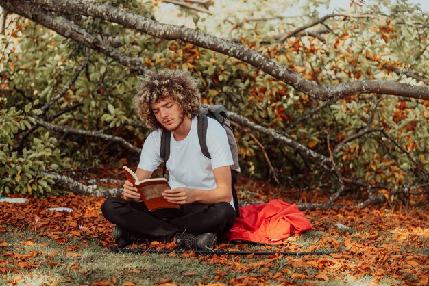 Un adolescent afro se détend en lisant un livre assis dans les bois par beau temps d'automne