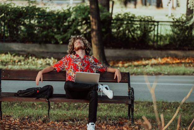 Un adolescent afro utilise un ordinateur portable pour une réunion en ligne tout en étant assis sur un banc de parc. Photo de haute qualité