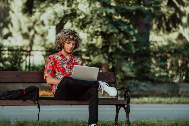 Un adolescent afro utilise un ordinateur portable pour une réunion en ligne tout en étant assis sur un banc de parc