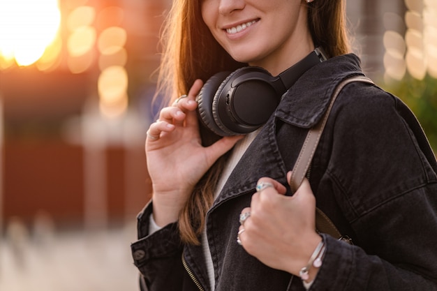 Adolescent aime et écoute de la musique dans des écouteurs sans fil noirs tout en se promenant dans la ville