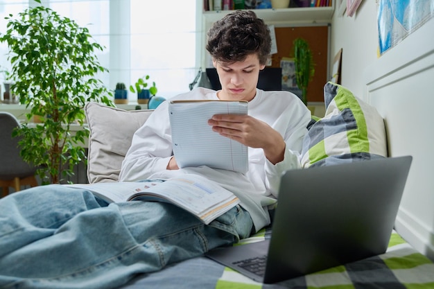 Photo un adolescent allongé à la maison sur le canapé, un étudiant utilisant un ordinateur portable, un cahier de notes, un manuel.