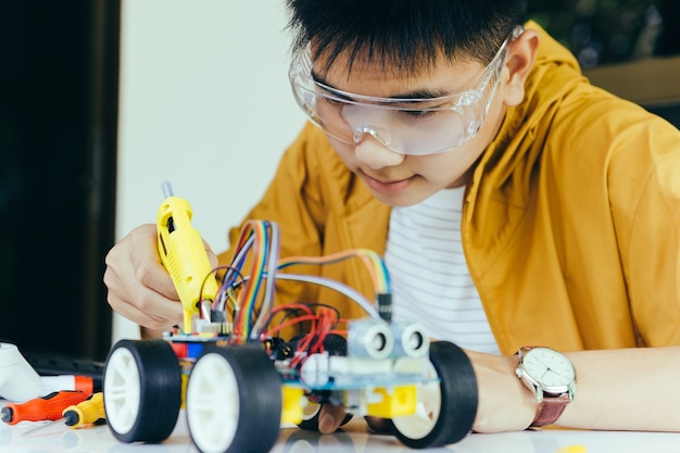 Adolescent asiatique branchant le câble d'énergie et de signal à la puce de capteur de l'atelier de voiture de jouet
