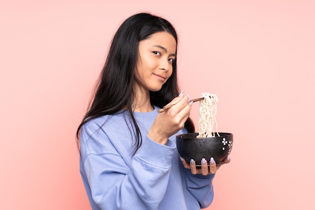 Adolescent asiatique femme isolée sur beige tenant un bol de nouilles avec des baguettes
