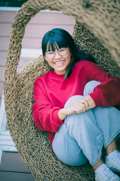 Adolescent asiatique à pleines dents souriant avec bonheur visage, détente sur berceau en bambou.