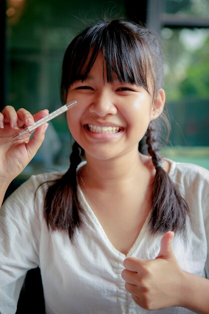 Adolescent asiatique à pleines dents souriant et tenant le thermomètre corporel dans la main