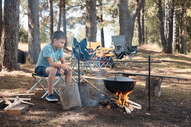 Adolescent assis autour d'un feu de camp dans la forêt en été Pique-nique familial à l'extérieur Vie de camping Cuisiner dans un chaudron en feu dans la nature