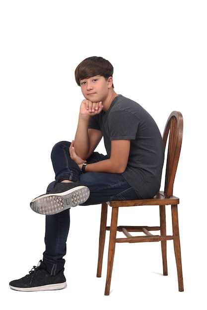 Adolescent assis sur une chaise avec un fond blanc, regardant la caméra et la main sur le menton