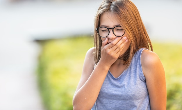 Adolescent bâille à l'extérieur tenant la main devant sa bouche.