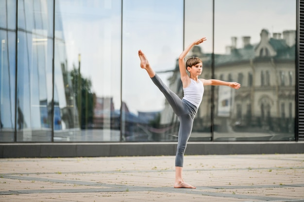 Adolescent de ballet dansant sur fond de reflet de la ville et du ciel dans le mur de verre