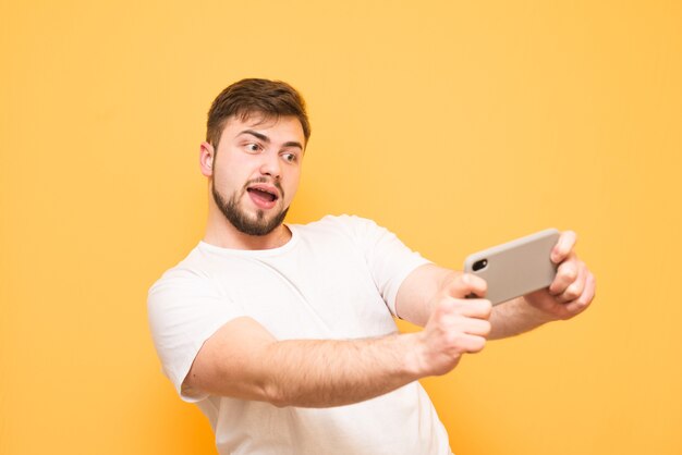 adolescent avec une barbe jouant expressivement à des jeux vidéo sur smartphone sur jaune.