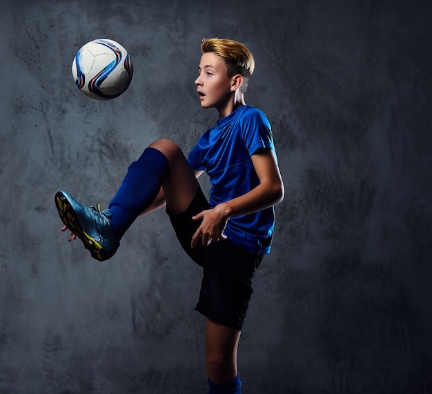 Adolescent blond, joueur de football vêtu d'un uniforme bleu joue avec un ballon.