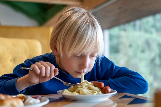 Adolescent blond à table en train de manger des pâtes Enfant garçon est en train de déjeuner Étudiant mangeant à la cafétéria de l'école