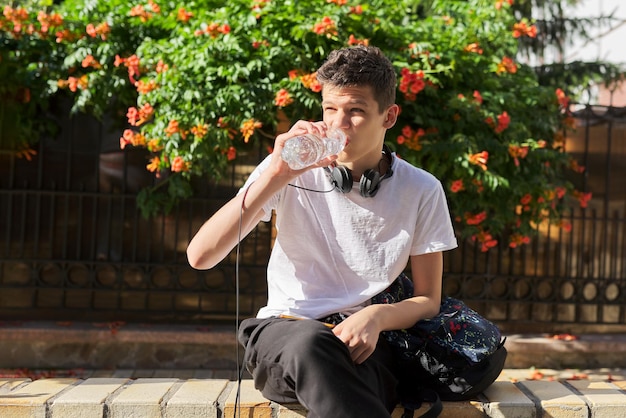 Un adolescent boit de l'eau de la bouteille et élimine la soif lors d'une chaude journée d'été dans la ville