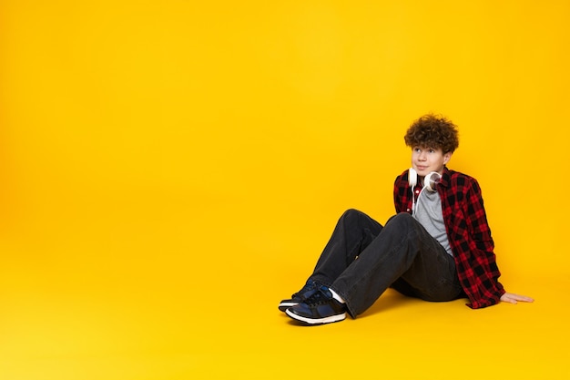 Photo un adolescent bouclé assis sur le sol sur un fond jaune
