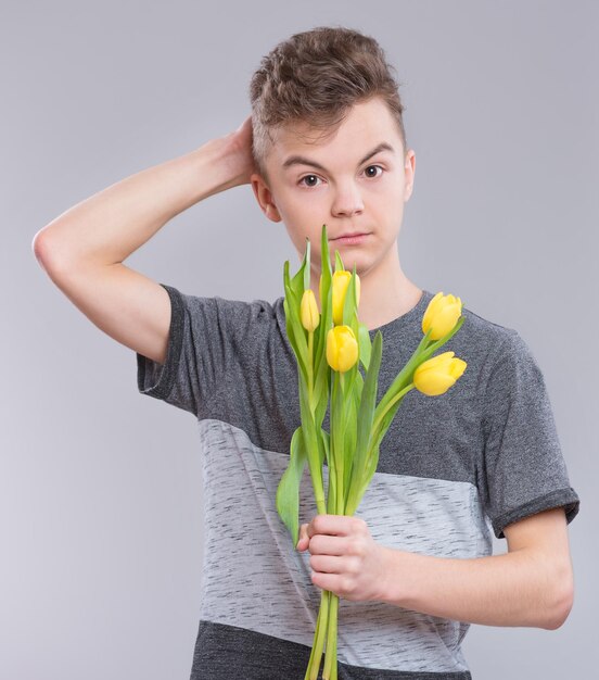 Photo adolescent avec un bouquet de fleurs sur fond gris enfant attentionné avec un bouchet de tulipes en cadeau joyeux anniversaire de mère ou jour de la saint-valentin