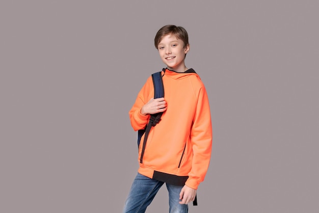 Un adolescent caucasien dans un sweat-shirt orange avec un sac à dos sur le dos posant