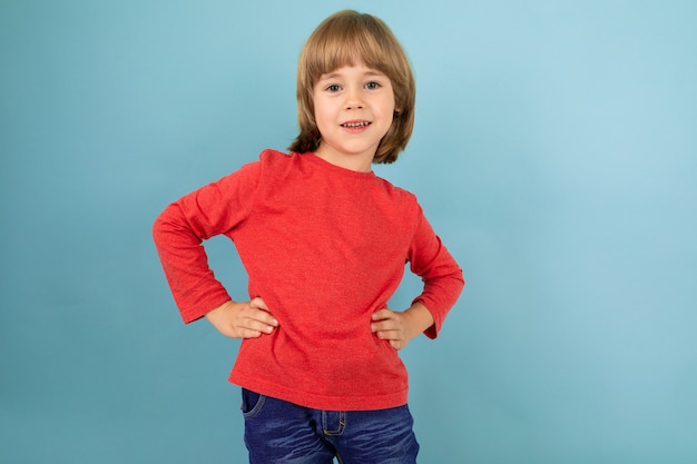 Un adolescent caucasien dans une veste rouge garder les mains sur sa ceinture, photo isolé sur bleu