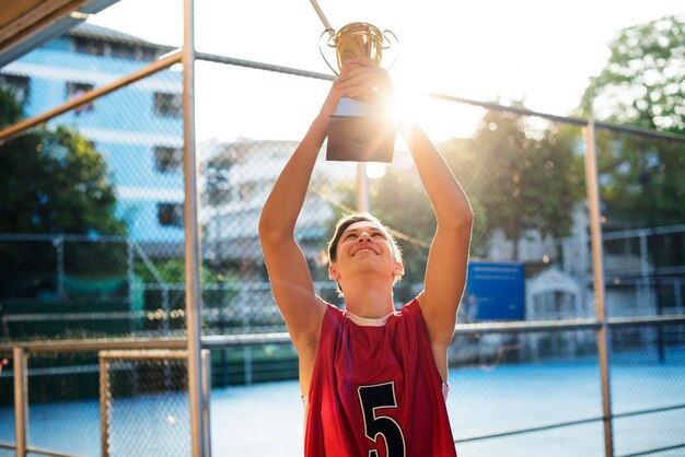 Adolescent caucasien dans des vêtements sportifs brandissant un trophée en plein air