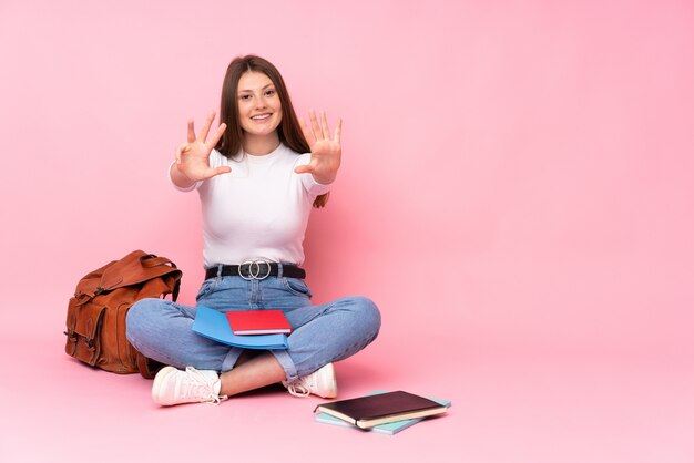 Adolescent caucasien étudiant fille assise sur le sol isolé sur rose en comptant neuf avec les doigts