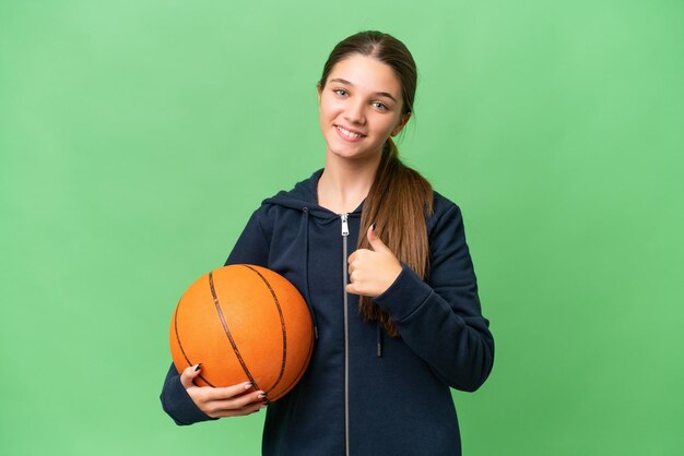 Adolescent caucasien fille jouant au basket-ball sur fond isolé donnant un coup de pouce geste