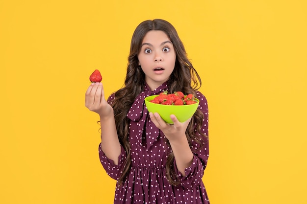 Un adolescent choqué tient un bol de fraises sur fond jaune