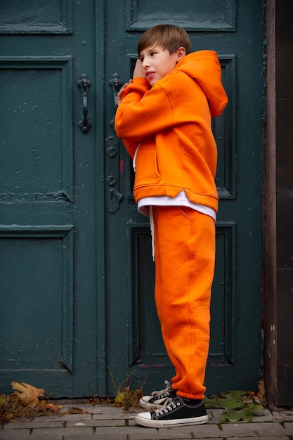 Photo un adolescent en costume orange se tient à la porte verte et écoute.