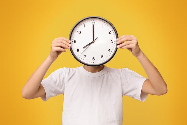 Un adolescent couvrant son visage avec une grande horloge panoramique orange