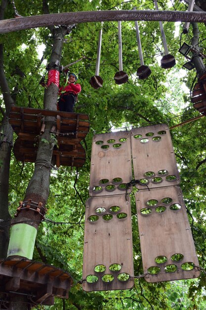 Un adolescent dans un casque de sécurité monte une échelle suspendue dans un parc d'attractions de corde