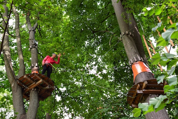 Un adolescent dans un casque de sécurité monte une échelle suspendue dans un parc d'attractions de corde