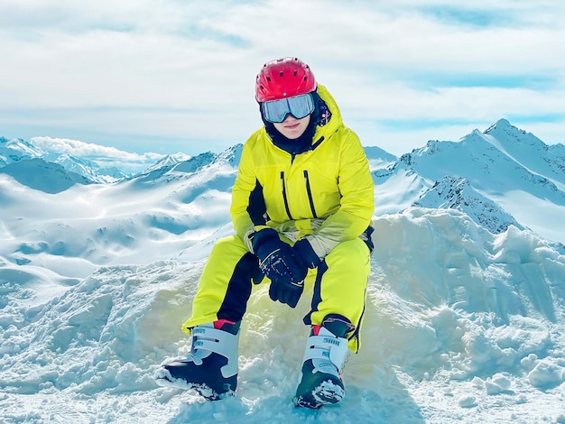 Photo un adolescent dans un costume de ski sportif brillant assis sur la neige dans les montagnes