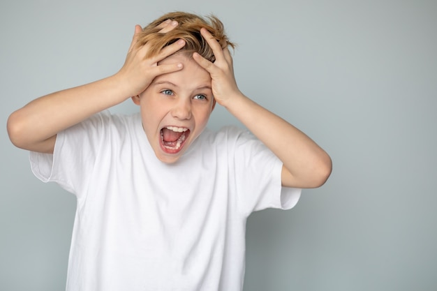 Un adolescent dans un Tshirt occasionnel crie tenant sa tête avec ses mains avec une expression agressive sur son visage des problèmes d'adolescence