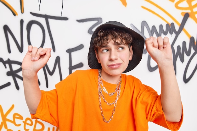 Un adolescent danse sur de la musique rap contre un mur d'art porte un chapeau noir et un t-shirt orange passe du temps libre dans un lieu public appartient à la culture des gangs