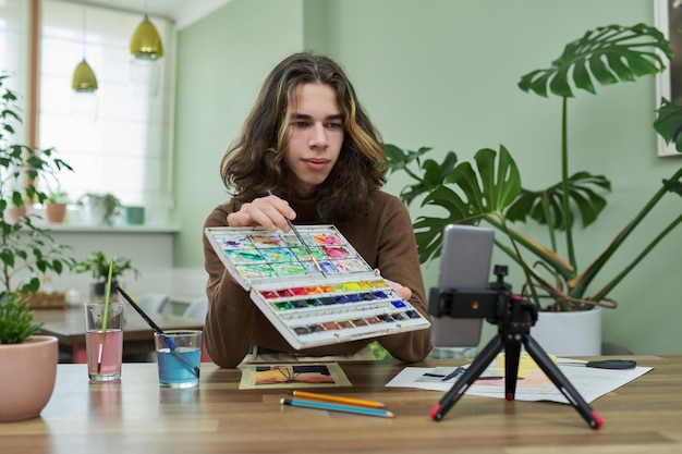 Un adolescent dessinant à l'aquarelle en regardant un cours vidéo sur un smartphone