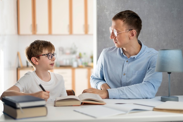 Un adolescent d'écolier et un jeune tuteur étudient à la maison. Le tuteur aide le garçon à faire ses devoirs. Enseignement à domicile