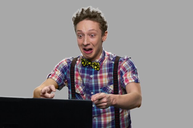 Adolescent émotionnel regardant l'écran du portable. Adolescent choqué expressif à l'aide de tablette informatique sur fond gris.