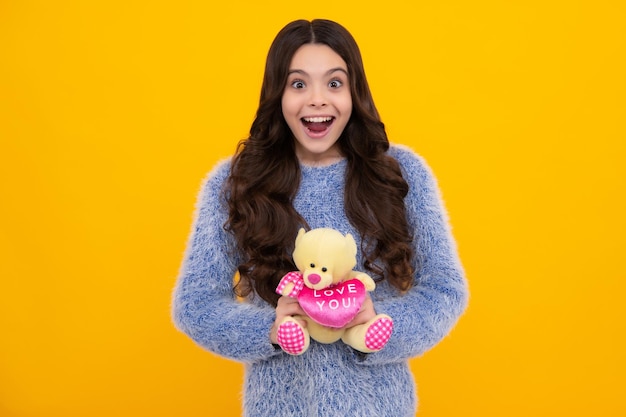 Adolescent enfant fille tenant un jouet en peluche isolé sur fond jaune enfance heureuse Enfant avec jouet ours en peluche avec coeur d'amour pour la Saint Valentin Heureux adolescent positif et souriant